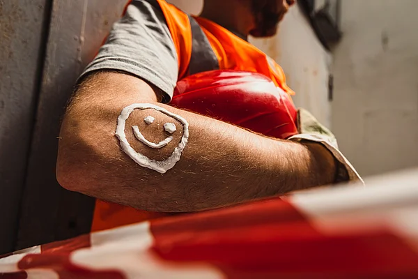 Ein Bauarbeiter trägt auf seinem Arm einen Smiley aus Sonnencreme auf.
