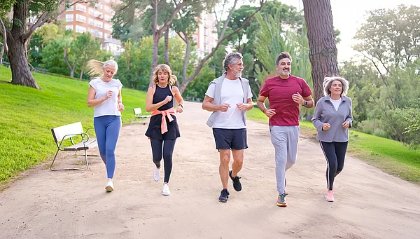 Fünf Erwachsene joggen gemeinsam auf einem Weg in einem Park.
