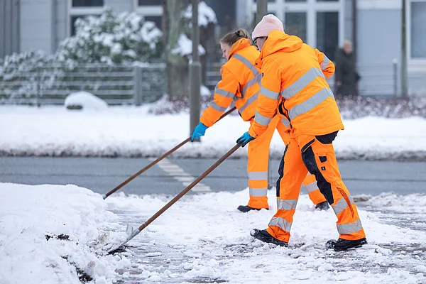 Zwei Beschäftigte der Stadtreinigung Hamburg in orangefarbener Sicherheitskleidung schieben Schnee.