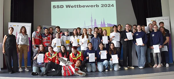 Eine große Gruppe von Schülerinnen und Schülern steht auf einer Bühne.