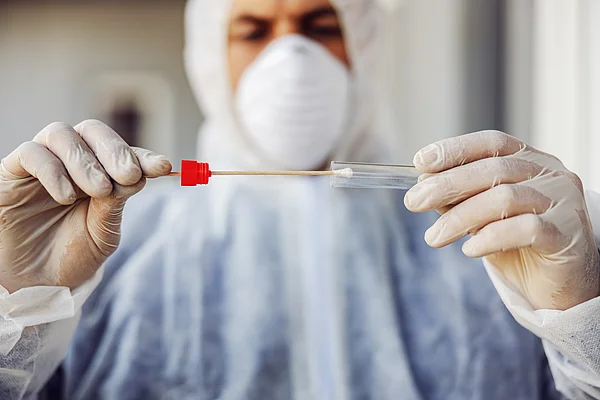 Mann mit Schutzanzug und Maske hält einen Corona-Test