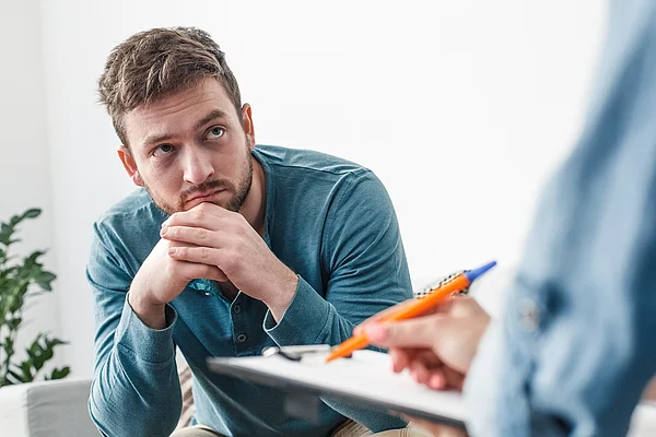 Junger Mann sitzt mit besorgtem Blick in Therapie