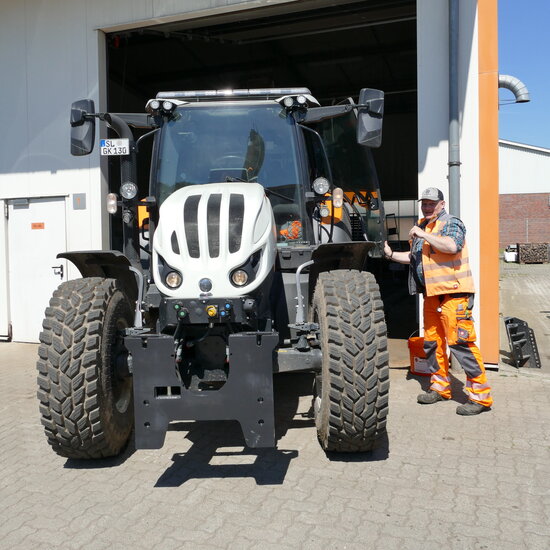 Mann in Arbeitsschutzkleidung steht neben Traktor