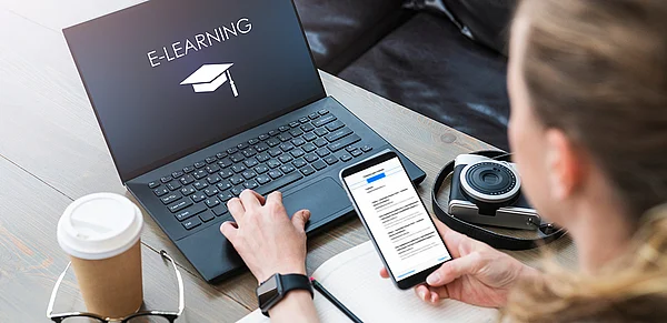 Junge Frau vor einem Laptop, auf dem Bildschirm steht E-Learning