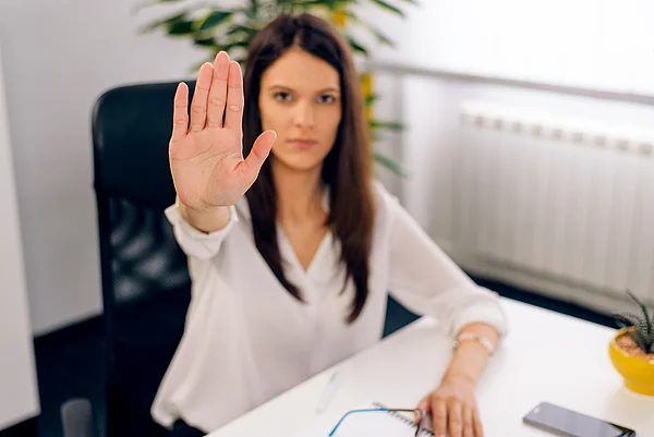 Eine Frau an einem Schreibtisch hebt abwehrend ihre Hand.