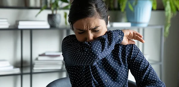 Frau niest in Armbeuge