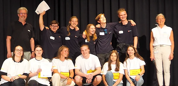 Zwei Schülergruppen in schwarzen bzw. weißen Shirts stehen auf einer Bühne.