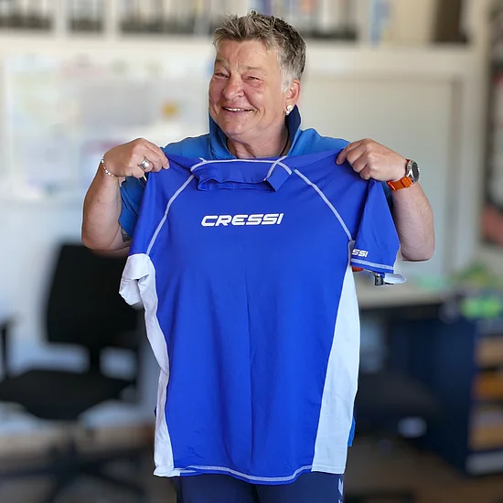 Eine Frau hält ein blaues T-Shirt aus UV-abweisendem Stoff hoch