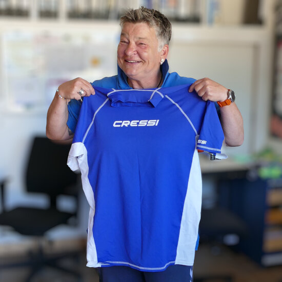 Eine Frau hält ein blaues T-Shirt aus UV-abweisendem Stoff hoch