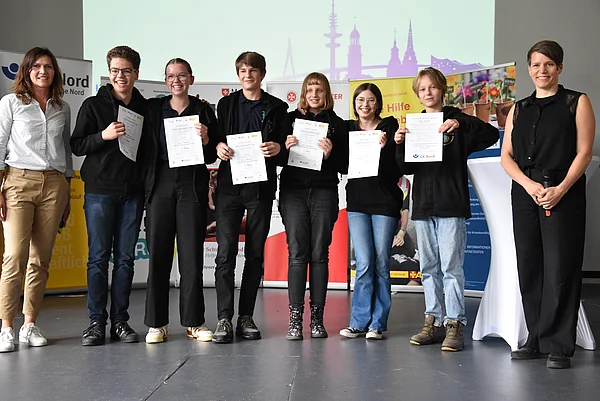 Sechs Schülerinnen bzw. Schüler und zwei erwachsene Frauen stehen auf einer Bühne.