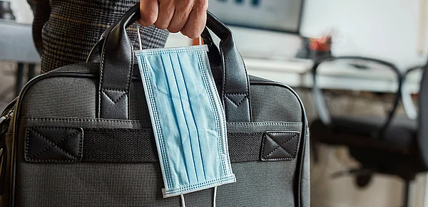 Person läuft mit Aktentasche und Maske in der Hand durchs Bild