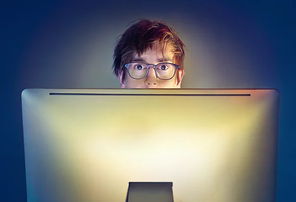 Ein junger Mann mit Brille blickt mit großen Augen über den Rand seines Bildschirms.