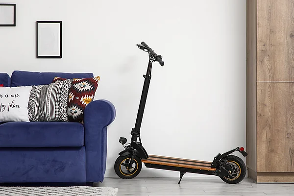 Elektro-Tretroller neben einem blauen Sofa.